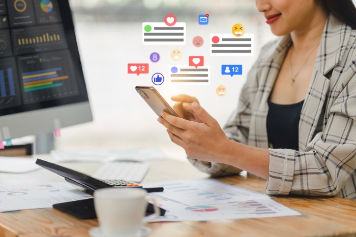 Mulher mexendo no celular com ícones de redes sociais aparecendo fora da tela.