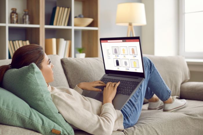 Uma mulher deitada no sofá, fazendo compras online no notebook.