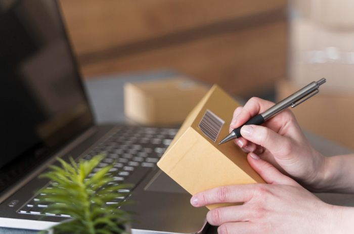 Pessoa assinando endereço em uma embalagem personalizada para enviar por transportadora.
