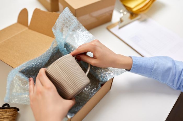 Xícara sendo colocada em uma caixa ideal para o tamanho do item, envolto em plástico bolha.